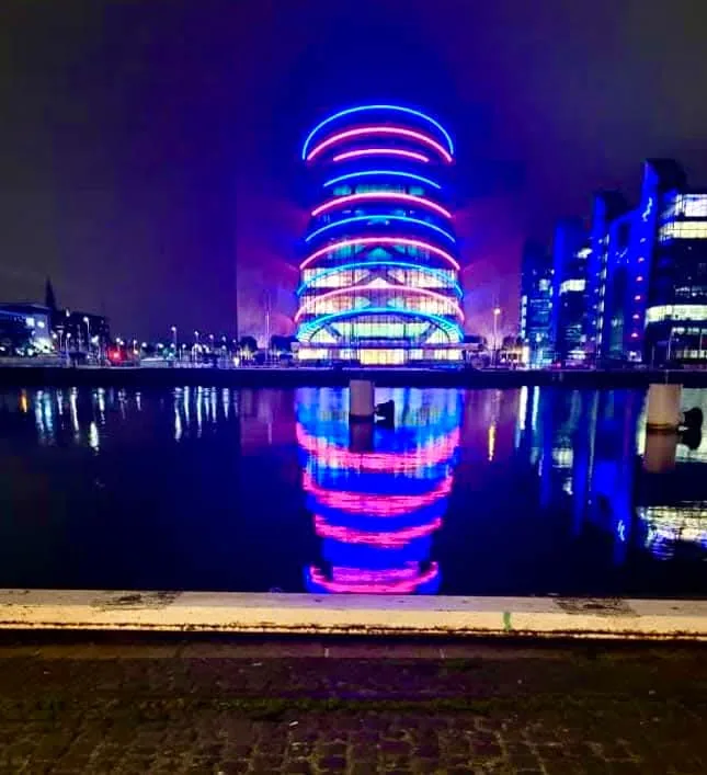 Blue and pink rings of light on the Convention Centre Dublin, mirrored in still water